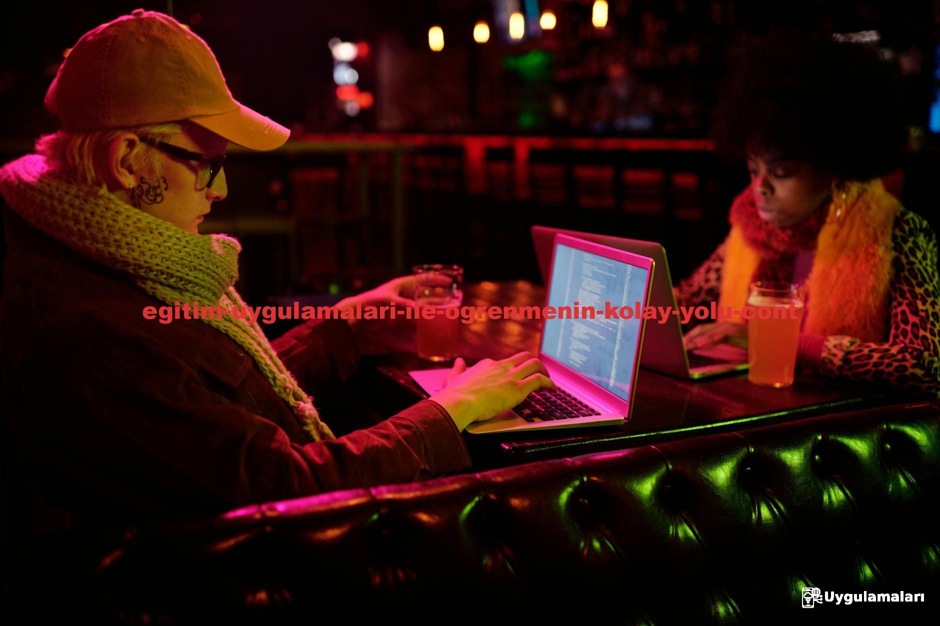 Two people coding on laptops in a bar setting, captured in a dim, creative atmosphere.