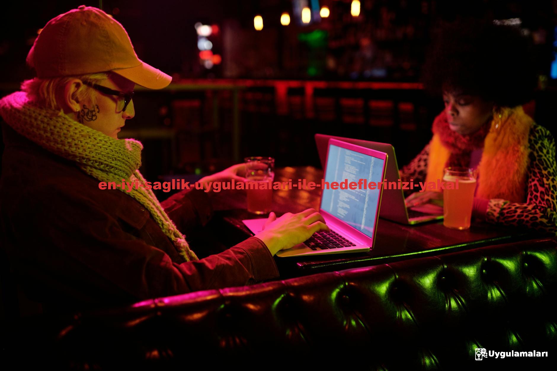 Two people coding on laptops in a bar setting, captured in a dim, creative atmosphere.