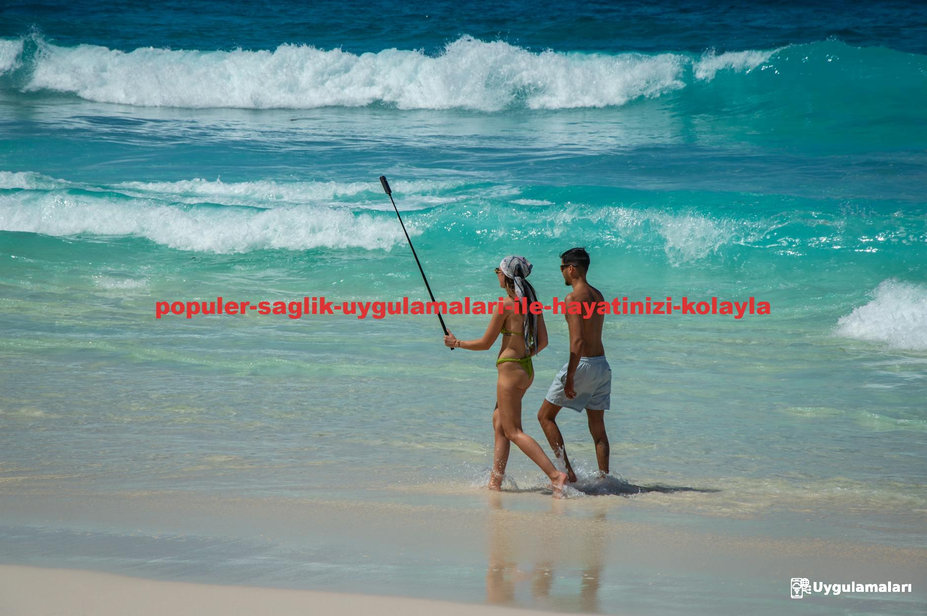 A couple enjoying a sunny day at the beach taking selfies with a selfie stick. Perfect for summer and vacation themes.