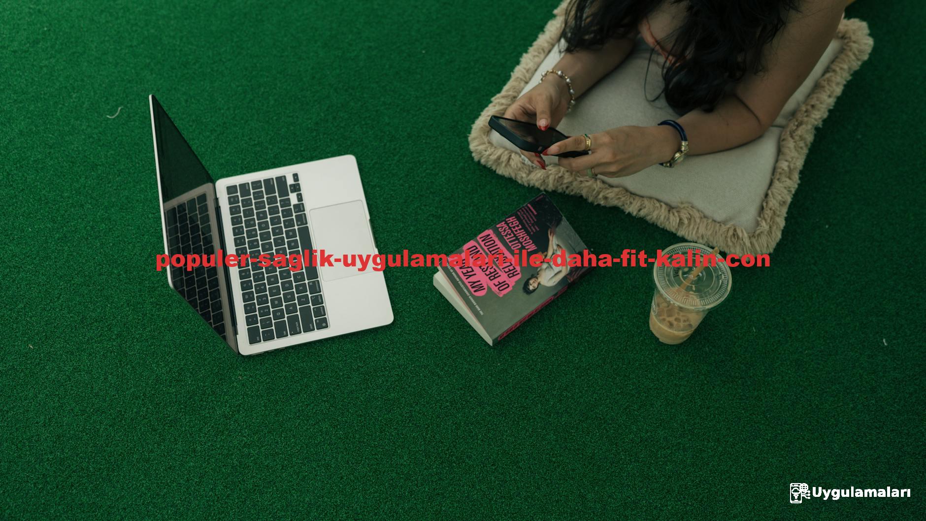 Woman using a smartphone by a laptop, book, and iced coffee on green turf.