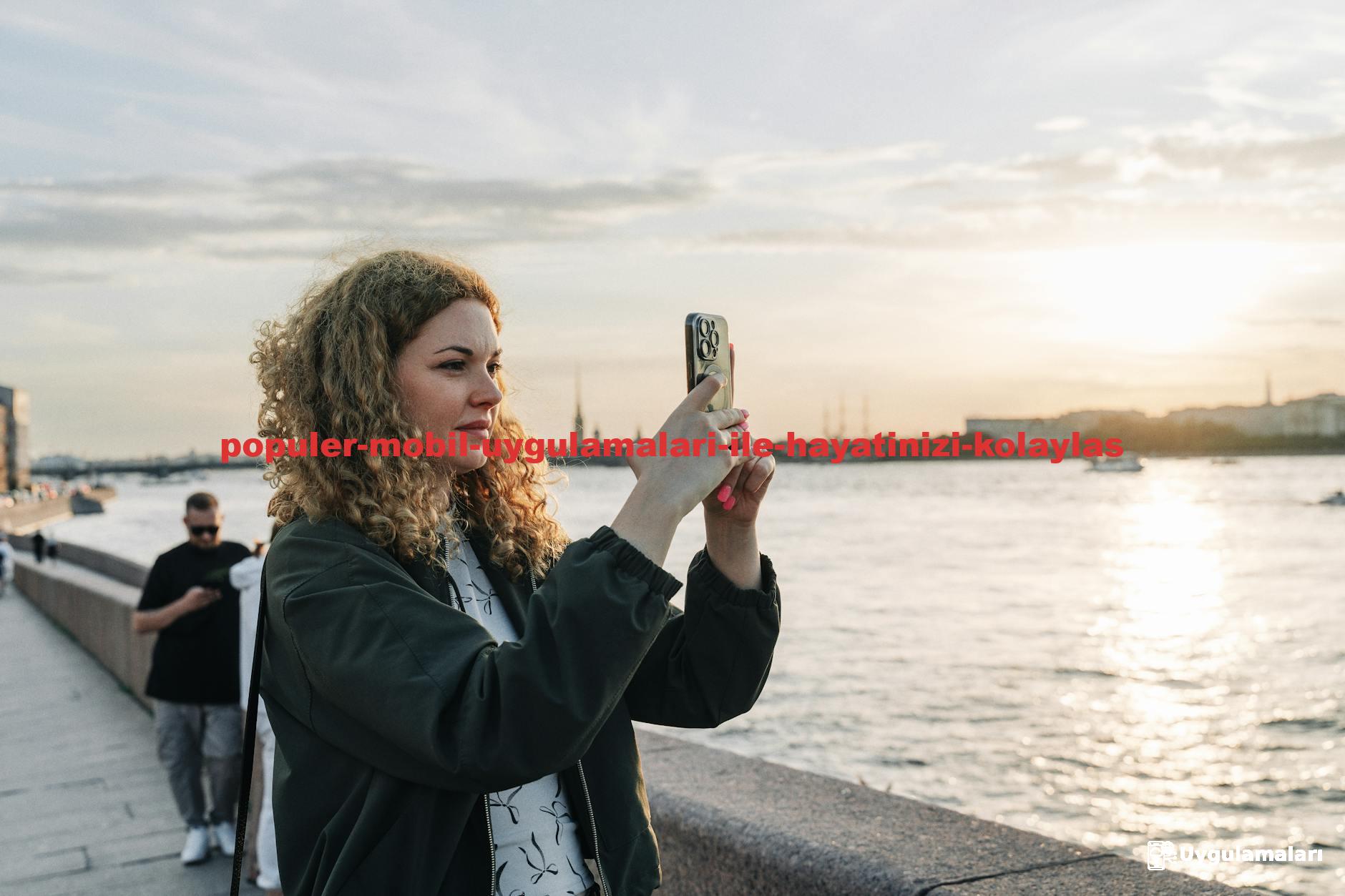 A woman captures sunset on her smartphone by the waterfront with scenic views.