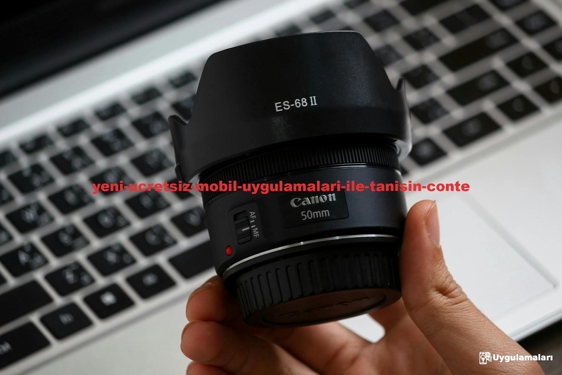 Detailed view of a Canon 50mm lens held over a laptop keyboard, showcasing tech accessories.