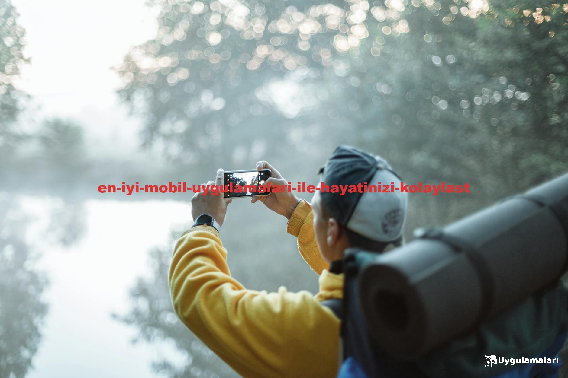 A man in a yellow jacket takes a photo of a misty lake with his smartphone in the morning outdoors.