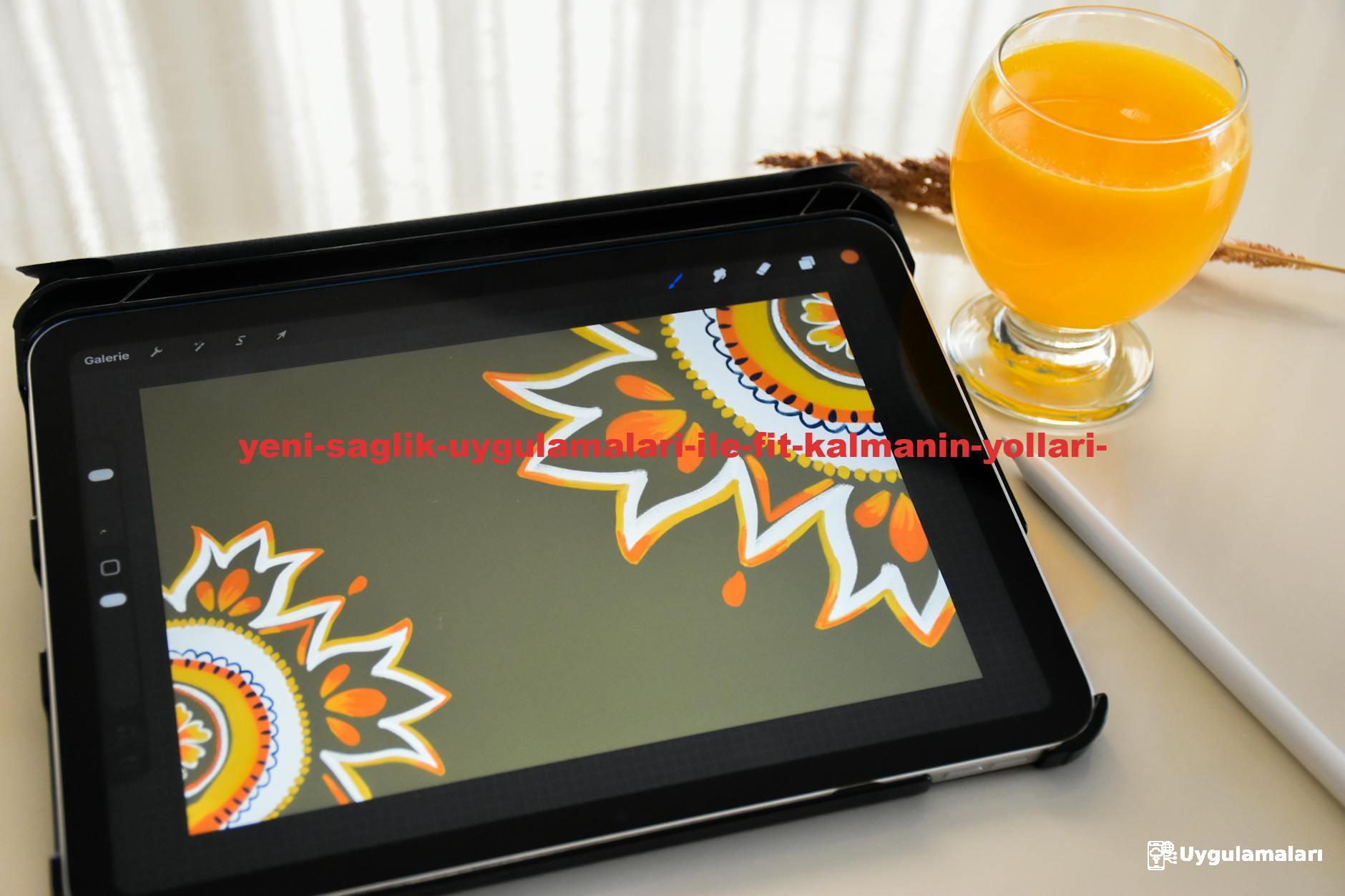A tablet displaying mandala artwork beside a glass of orange juice on a table.